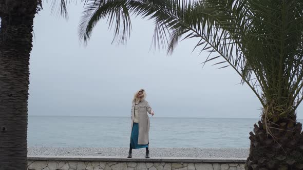 stylish woman dancing on the beach among palm trees in cloudy weather