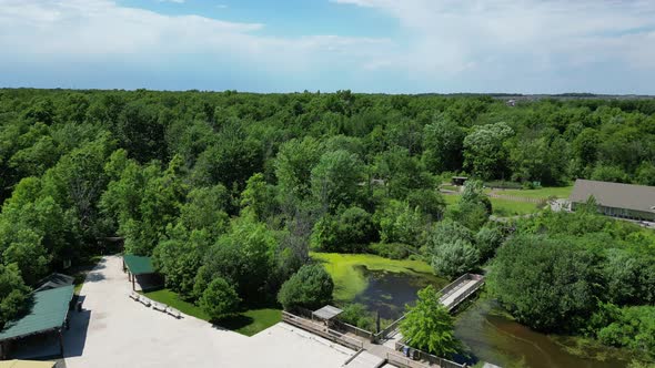 Static aerial of forest park camp during summer with bridge crossing algae pond alt