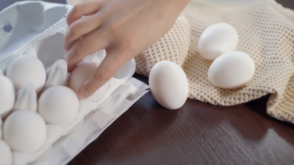 Chicken Eggs In Carton On Kitchen Table. Hand Takes Out Eggs From Carton alt