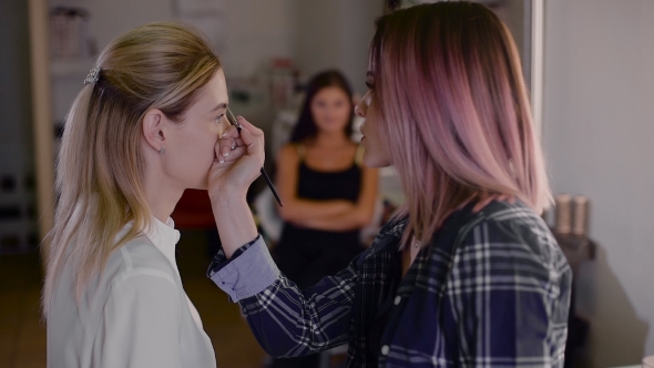 Girl Stylist Working In a Beauty Studio. Make-up For a Beautiful Blonde. Working With Shadow alt