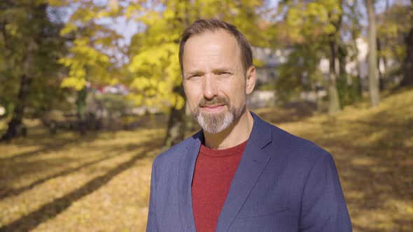 A Middleaged Handsome Caucasian Man Smiles at the Camera in a Park in Fall  Closeup