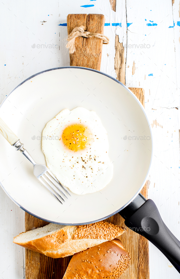 Fried egg with spice and bread slices in white ceramic frying pan on wooden  board Stock Photo by sonyakamoz