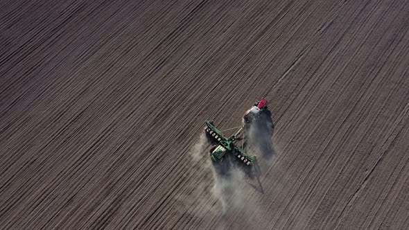 Aerial view of tractor with harrow system plowing ground on cultivated farmfield alt