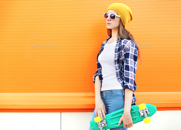 Fashion pretty girl with skateboard over colorful orange backgro