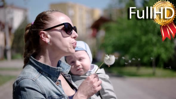 Young Woman With Her Baby Son Blows Dandelion alt