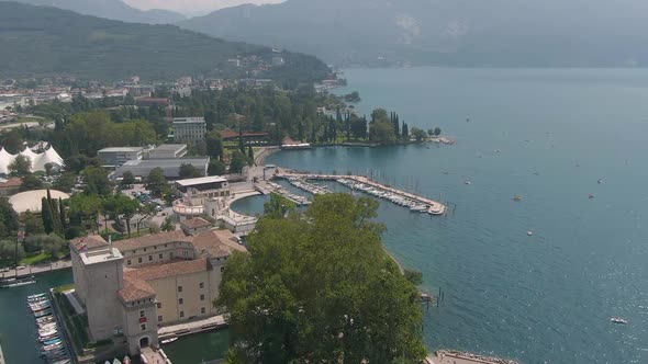 Beautiful drone shot of the harbor in Riva del Garda with an old castle in the foreground and the la alt