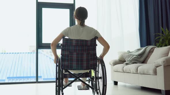 A Young Woman in a Wheelchair Drives Up to the Window and Looks Outside alt