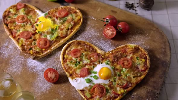 Two Heart-Shaped Pizzas and Two Glasses of White Wine on a Wooden Board Ready for a Romantic Dinner alt
