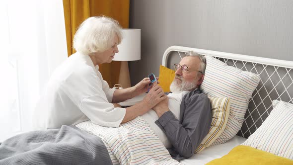 Elderly Woman Apply at Sick Husband's Fingertip Pulse Oximeter Check Pulse Rate