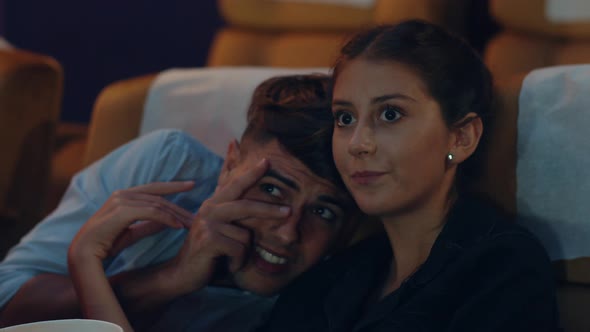 Attractive cheerful young caucasian woman watching horror movie in cinema theater. alt