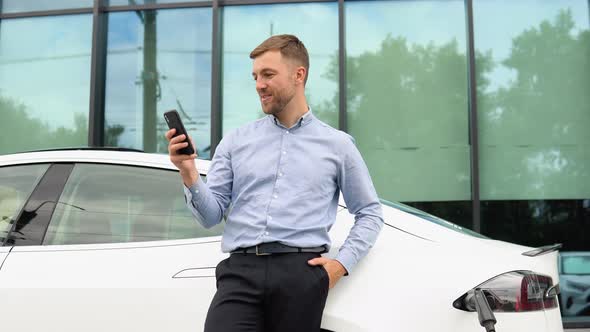 Portrait of Young Handsome European Man Speaking on a Video Chat on His Smartphone While Leaning on alt