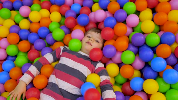Little boy playing in the pool with plastic balls in the nursery. The kid is swimming alt