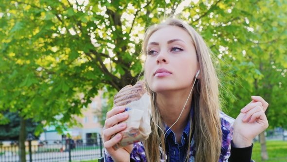 Attractive Woman Eating a Sandwich In The Park, Listening To Music alt