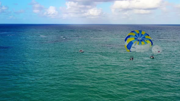 Two people parasailing together in yellow and blue parachute in open green ocean waters, circle aeri alt