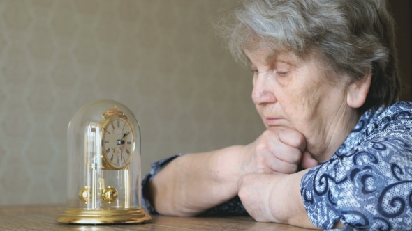 Old Woman Looks At The Table Clock With Pendulum