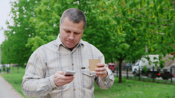 Middle-aged Man Drinking Coffee On The Go, Walking On City Park alt