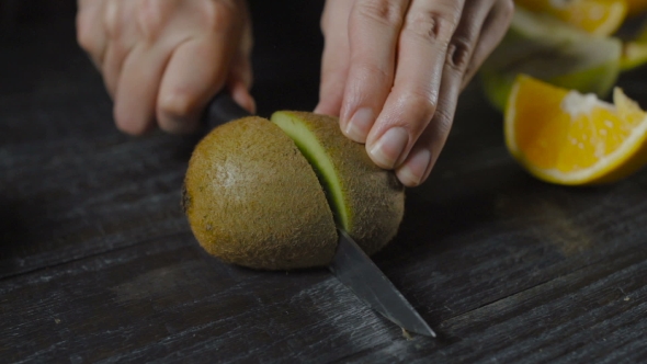 Chef Cuts Kiwi With Knife On Dark Wooden Table alt