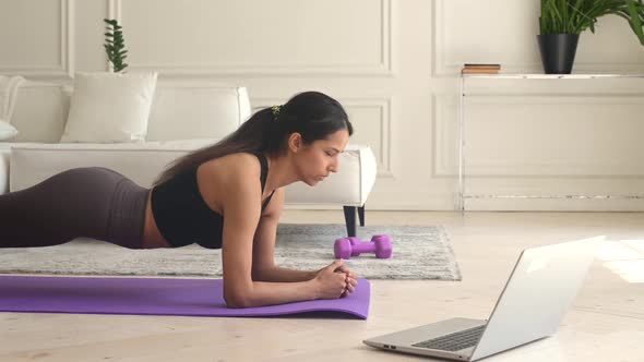Indian Young Woman Using Laptop for Watching Sports Video Tutorial Doing Plank