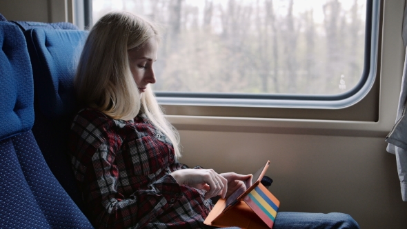 Young Woman Using Tablet In Colourful Case While Traveling By Train