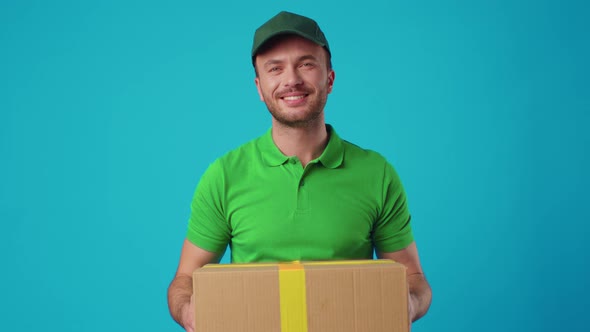 A Young Male Courier in a Green Uniform Holds a Parcel in His Hands
