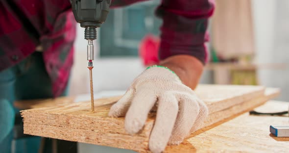 Concentrated Young Bearded Carpenter Wearing Jeans and a Plaid Flannel Shirt Drilling a Hole in a alt