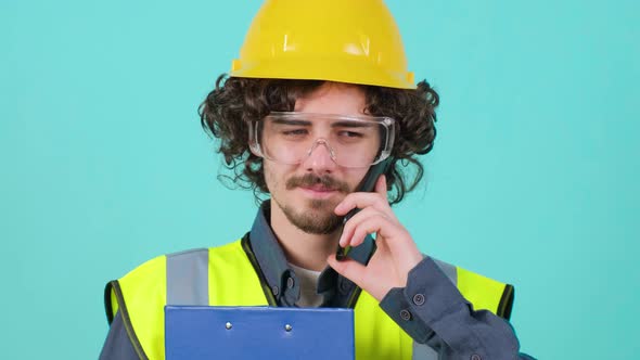 Construction Worker with Safety Glasses and Helmet That is Talking on Mobile Phone alt
