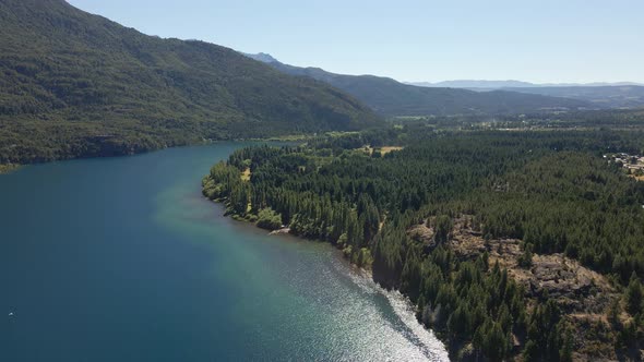 Aerial lowering on Epuyen lake between mountains covered in pine tree forest, Patagonia Argentina alt