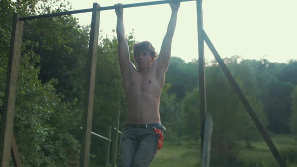 Young fit topless man doing knee raise exercise to strengthen core outdoor gym SLOW MOTION alt