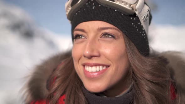 Portrait of a woman smiling lifestyle in the snow at a ski resort with goggles and beanie hat alt