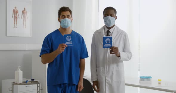 Portrait of Diverse Doctor and Nurse in Safety Mask Show Vaccination Passport Looking at Camera alt