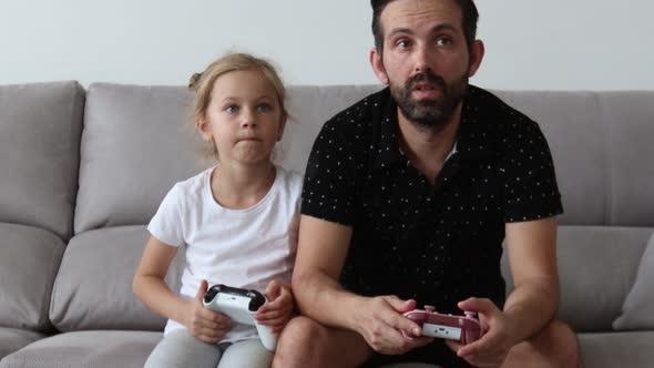 Father and Young Child are Playing Video Game on Couch at Home Pressing Buttons on Joystick