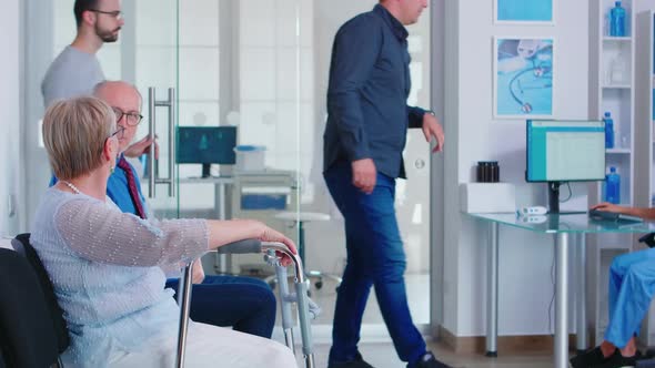 Disabled Senior Woman Talking with Old Man in Hospital Waiting Room alt