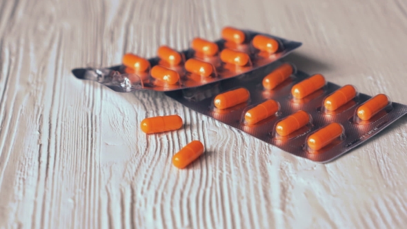 The Pills In Orange Capsules Fall On a White Table alt