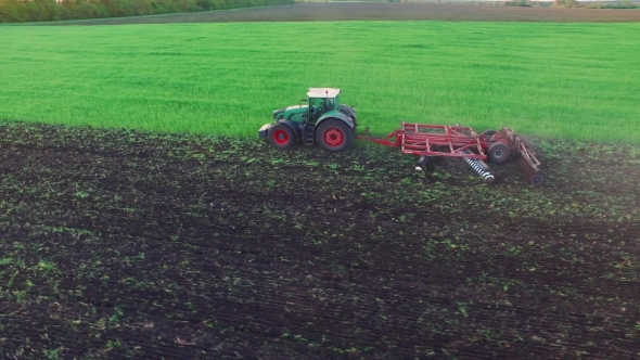 Tractor Plowing The Field, The Young Wheat Is Processed At The Fertilizer alt