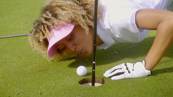 Young Woman Blowing Her Golf Ball Into The Hole alt