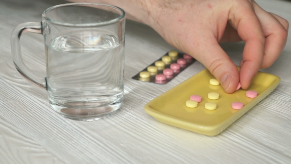 Man's Hand Takes The Pills From a Yellow Container alt