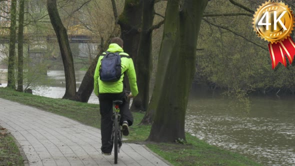 Man is Riding a Bicycle Along River Park Alley
