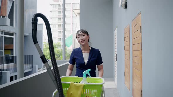 Asian hotel maid with trolley containing tools and accessories for cleaning room