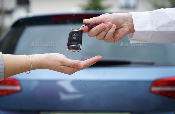 car dealer gives the customer the car keys with car in backgorun