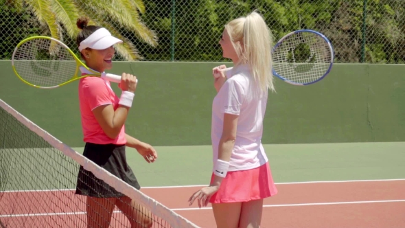Pair Of Friends Talking On Tennis Court alt