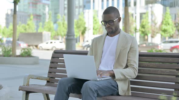 Rejecting African Man in Denial While Using Laptop Sitting Outdoor on Bench alt
