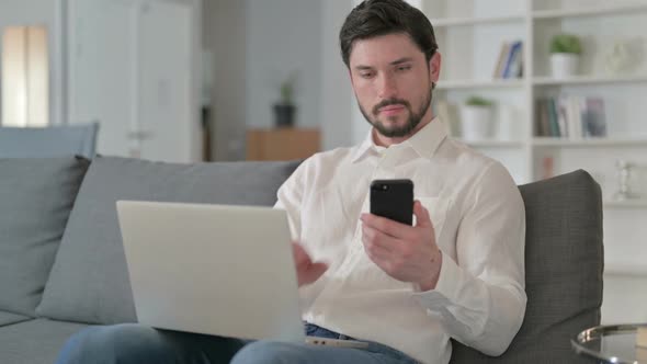 Focused Businessman Working on Smartphone and Laptop at Home alt