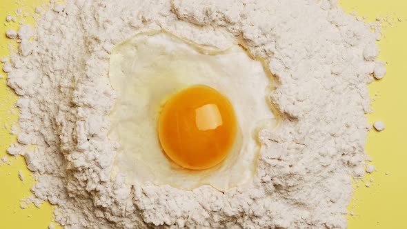 Broken egg yolk on flour for the dough on yellow background alt