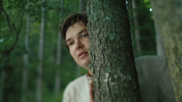 Young Carpathian Peasant Watching Someone in the Mountain Forest and Hiding By the Trees