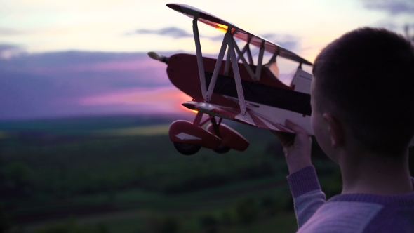 Boy Holds Homemade Airplane On Sunset Background On Rock.  alt