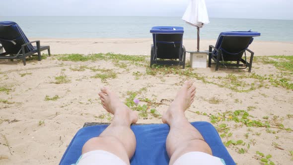 POV to man's legs, feet while relaxing on sunbed near beach in resort in thailand for sun bathing ta alt