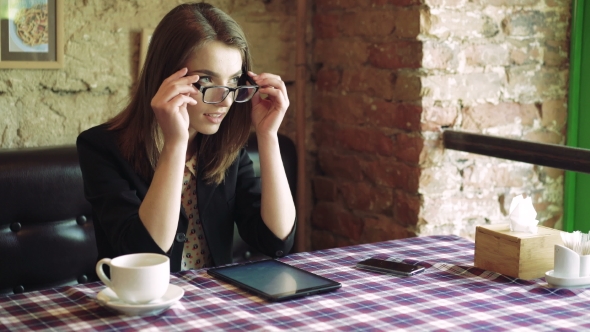 Business Lady In Glasses Drinking Coffee, Using a Tablet And Smiling In Cafe  alt