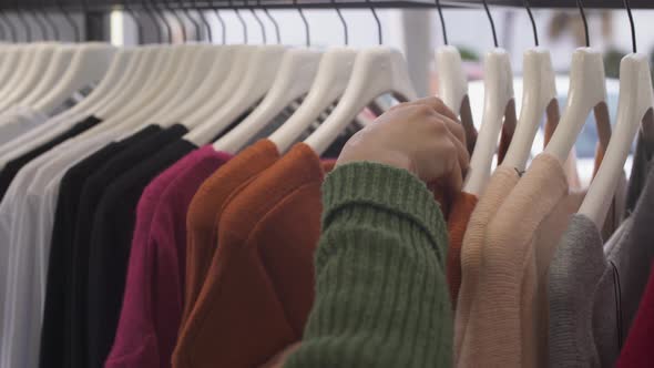 Closeup of Woman's Hand Picking Sweater From Fashion Boutique Rack