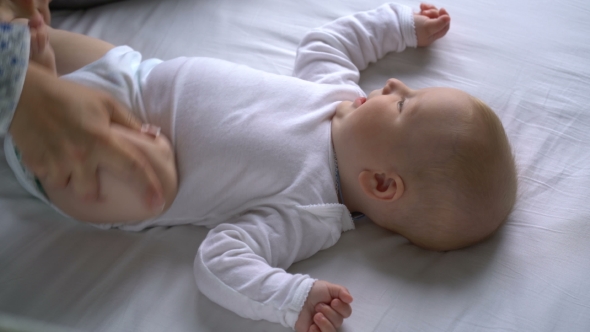 Mother Tickles The Baby And He Laughs Lying On The Bed alt