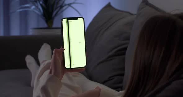 Young Woman Rests on the Sofa and Uses Smartphone Scrolls Through the Images and Swipe Across the alt